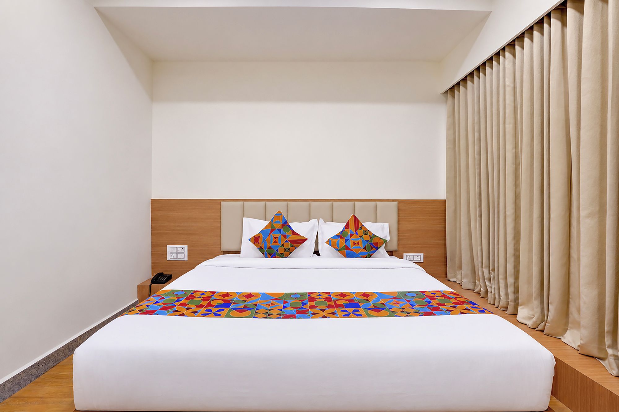 A hotel room with a large bed, a headboard, a nightstand, and a window with curtains.