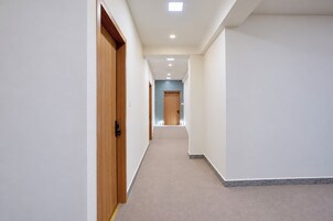 Un pasillo estrecho con una puerta de madera a la izquierda, una puerta azul claro al final y suelo alfombrado.