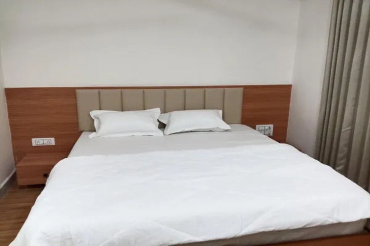 Quarto de hotel com cama, cabeceira e cortinas.