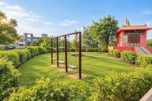 Un jardín bien cuidado con un columpio, una pequeña estructura roja con escalones, y un edificio con señalización 'INFINITE' al fondo.