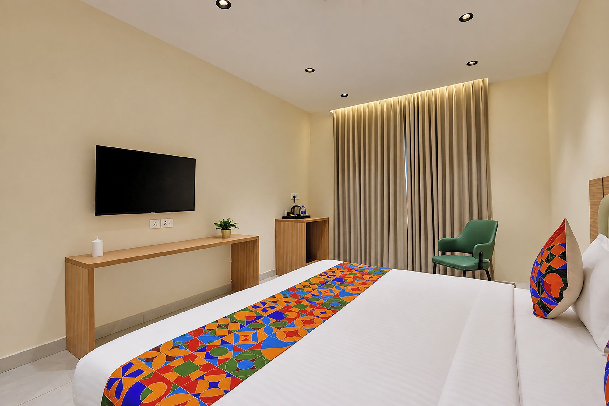 Une chambre d’hôtel avec un lit, un téléviseur fixé au mur, un bureau, une chaise et une grande fenêtre avec des rideaux.