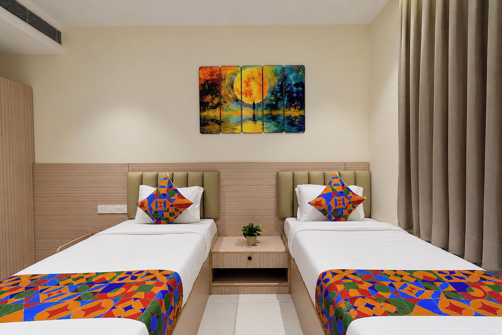 Quarto de hotel com duas camas, mesa de cabeceira, uma planta pequena e um quadro na parede.