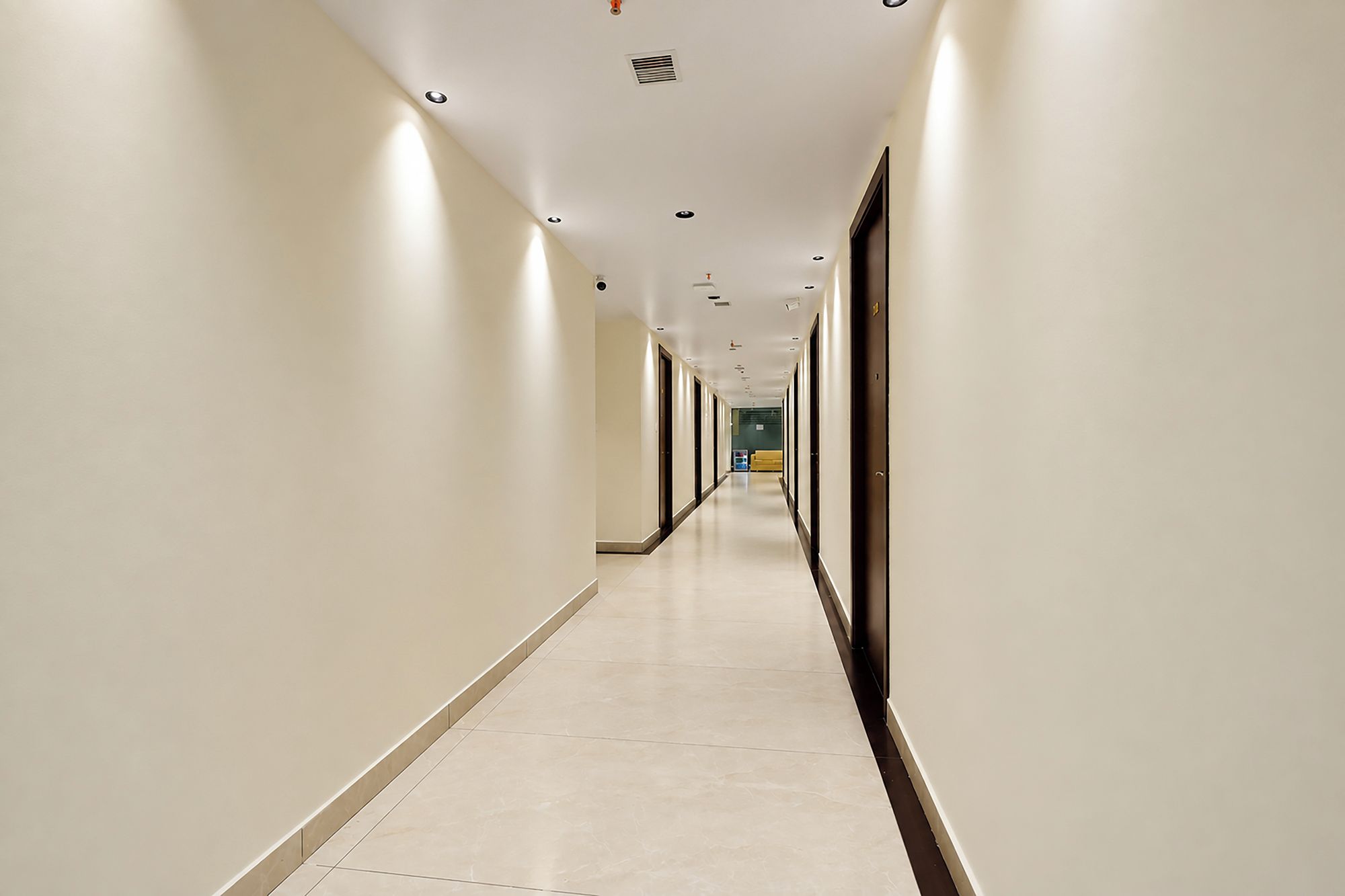 Corredor longo e estreito de um hotel, com portas em ambos os lados, que leva a um quarto no final.