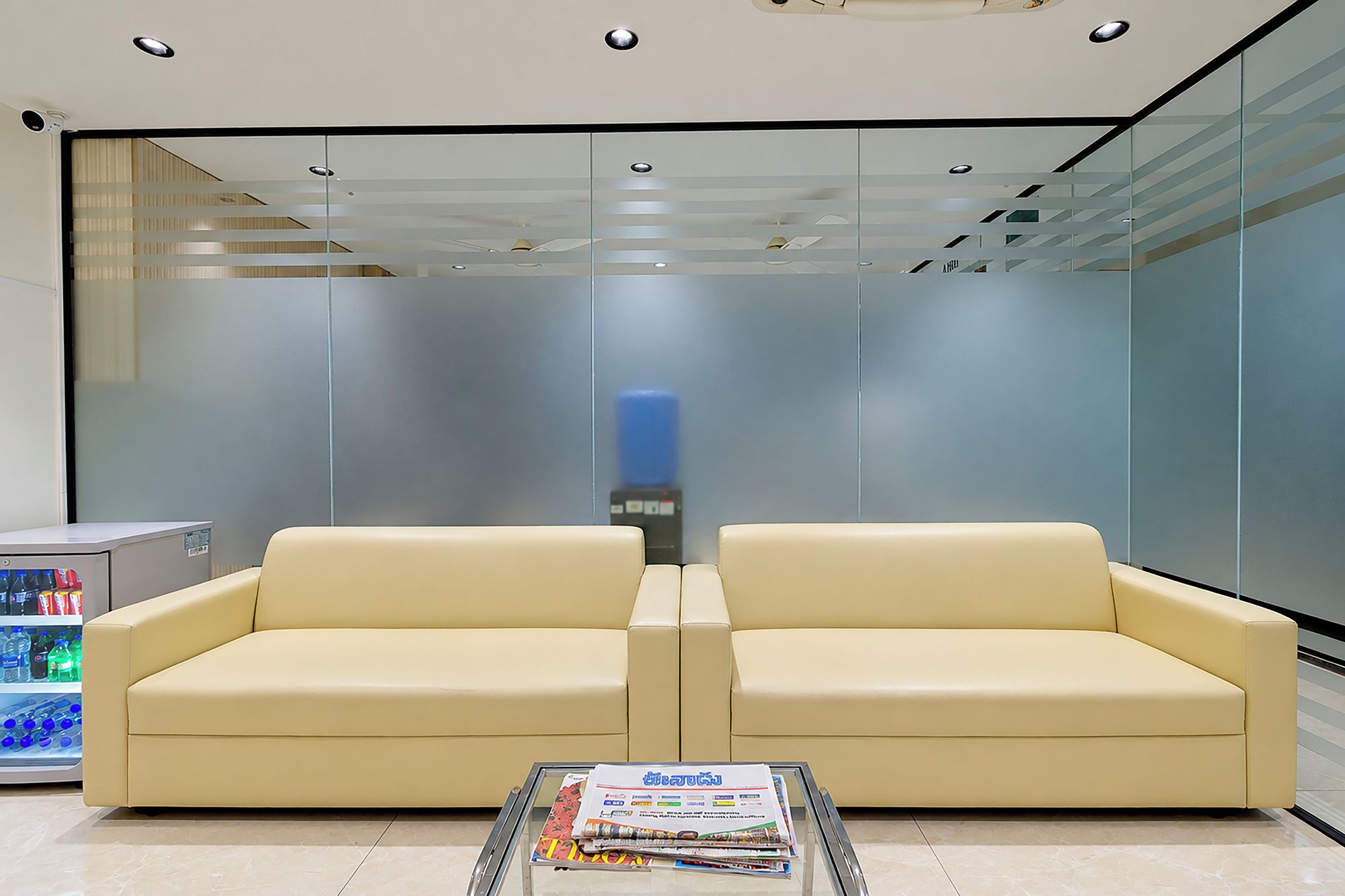 Un espace d’attente moderne comprenant deux canapés, une table en verre avec des magazines et un distributeur automatique.