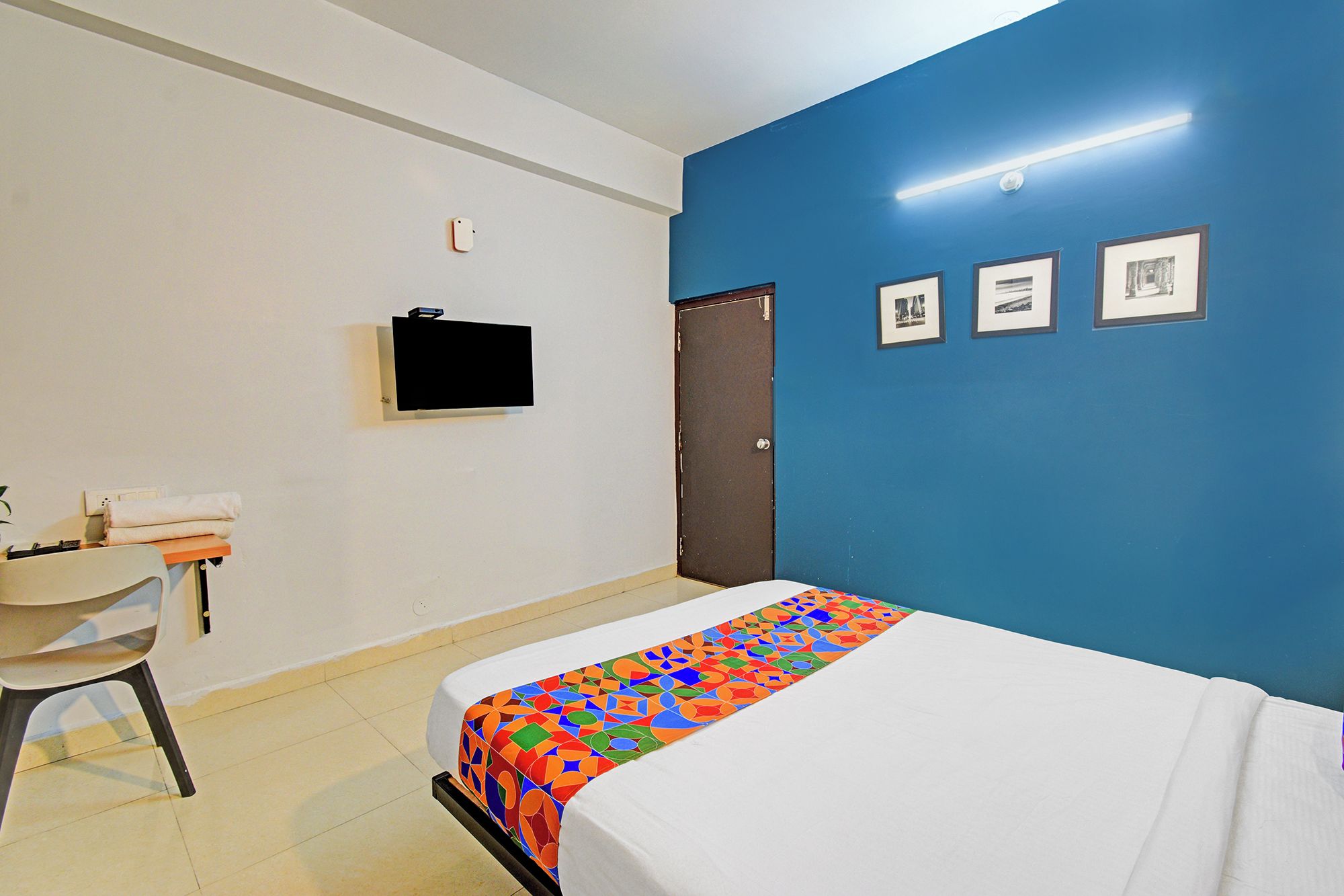 Habitación de hotel con cama, escritorio, silla, televisión montada en la pared y una puerta.