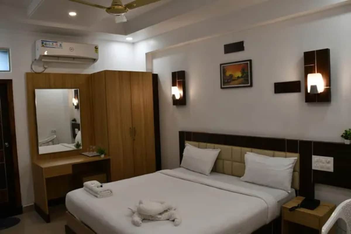 Habitación de hotel con cama, mesita de noche, espejo, armario e iluminación en la pared.