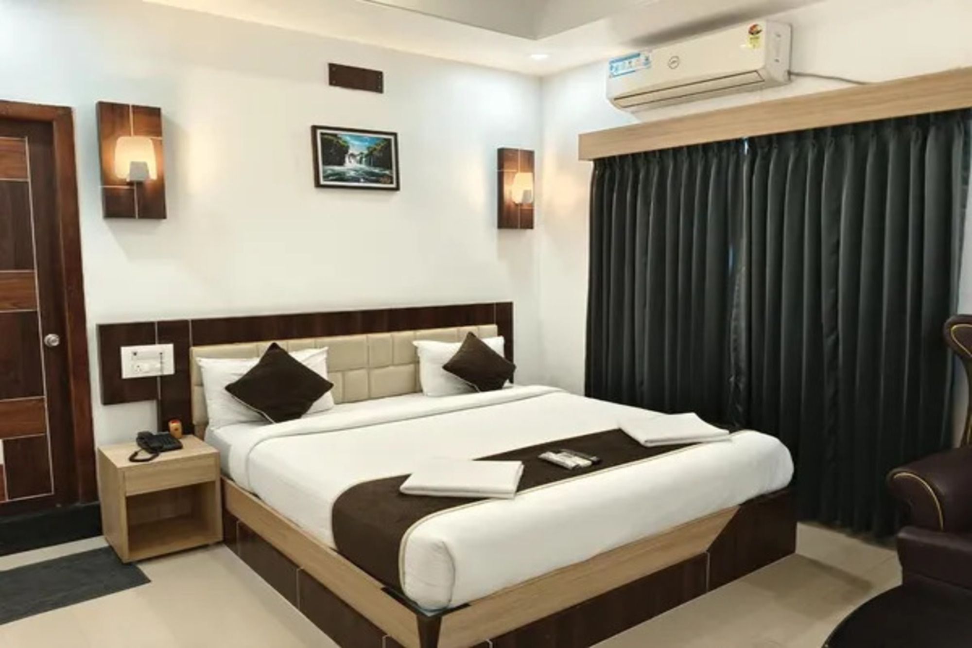 Una camera d'albergo con un letto grande, comodini, una scrivania, una sedia, un condizionatore d'aria a muro e una finestra con tende.