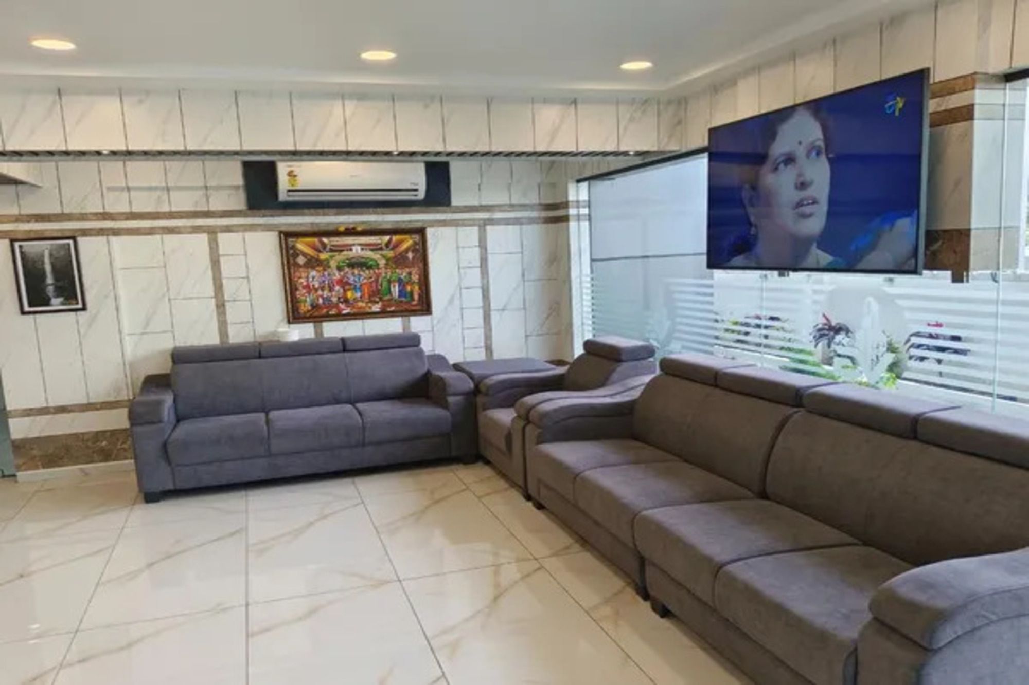 Een woonkamer met een hoekbank, een flatscreen-televisie aan de wand en een groot raam met zonwering.