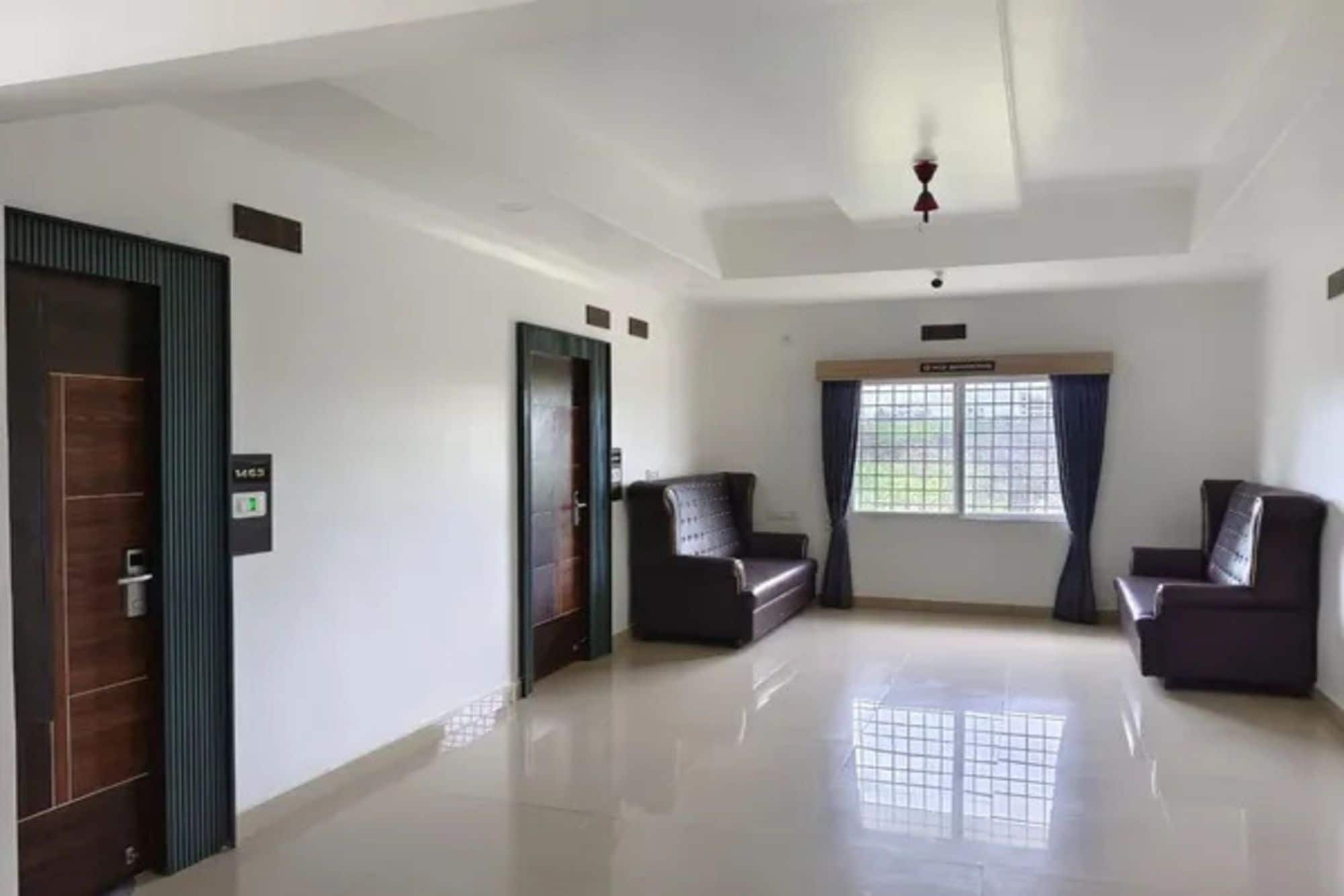 Una habitación amplia con techo alto, dos sofás de color oscuro, un ventanal con cortinas y una puerta con pantalla digital.