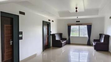 Una habitación amplia con techo alto, dos sofás de color oscuro, un ventanal con cortinas y una puerta con pantalla digital.