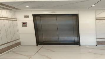 Un ascensore moderno con parete e pavimento in marmo, un pannello di controllo con una luce rossa e un logo sulla parete.
