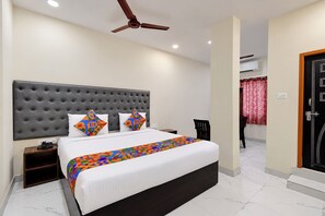 Una habitación de hotel con una cama grande, un ventilador de techo, una mesita de noche y una silla.