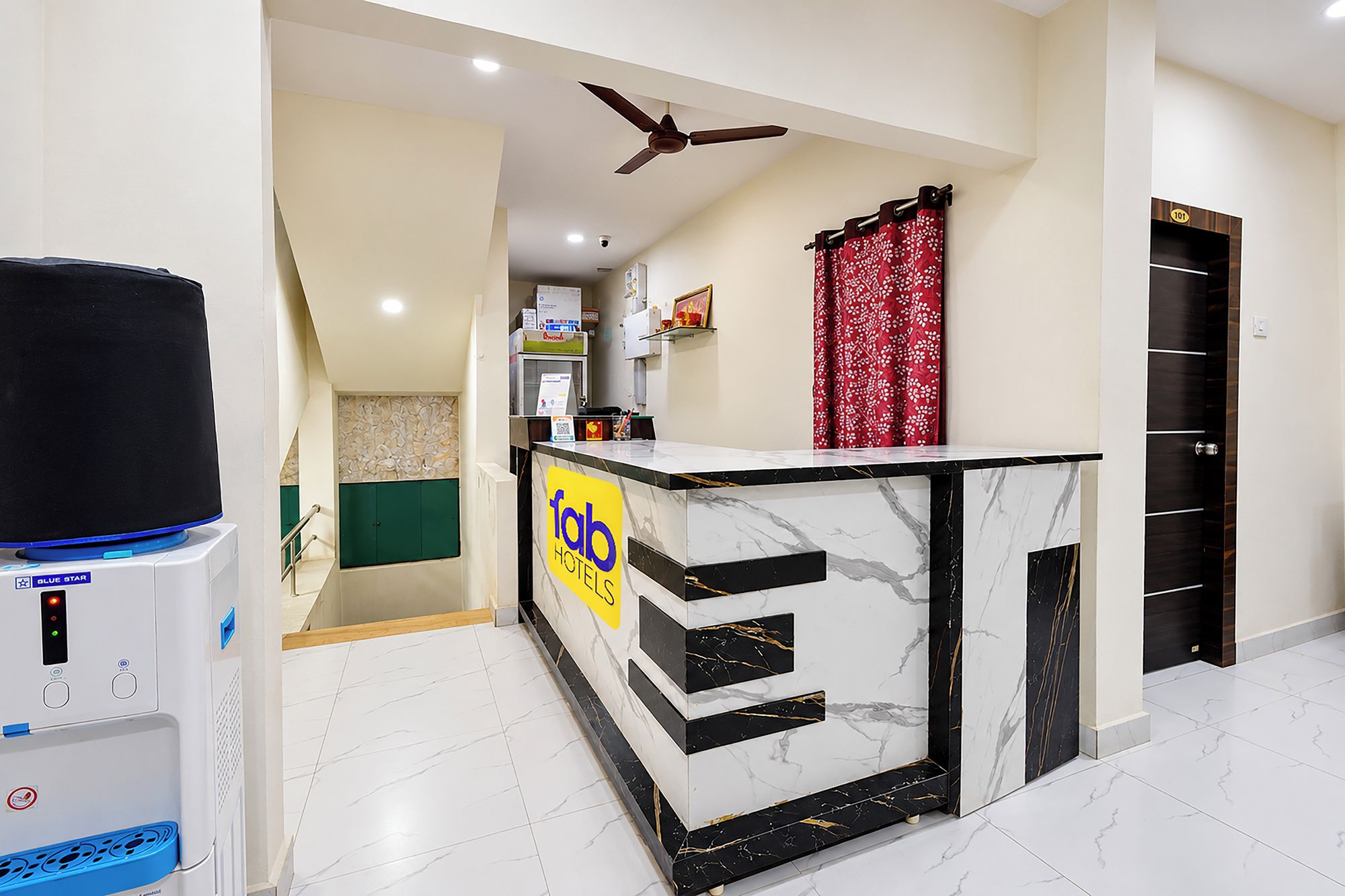A hotel reception area with a marble counter, a water dispenser, a ceiling fan, and a red curtain.