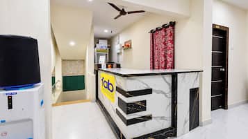 A hotel reception area with a marble counter, a water dispenser, a ceiling fan, and a red curtain.