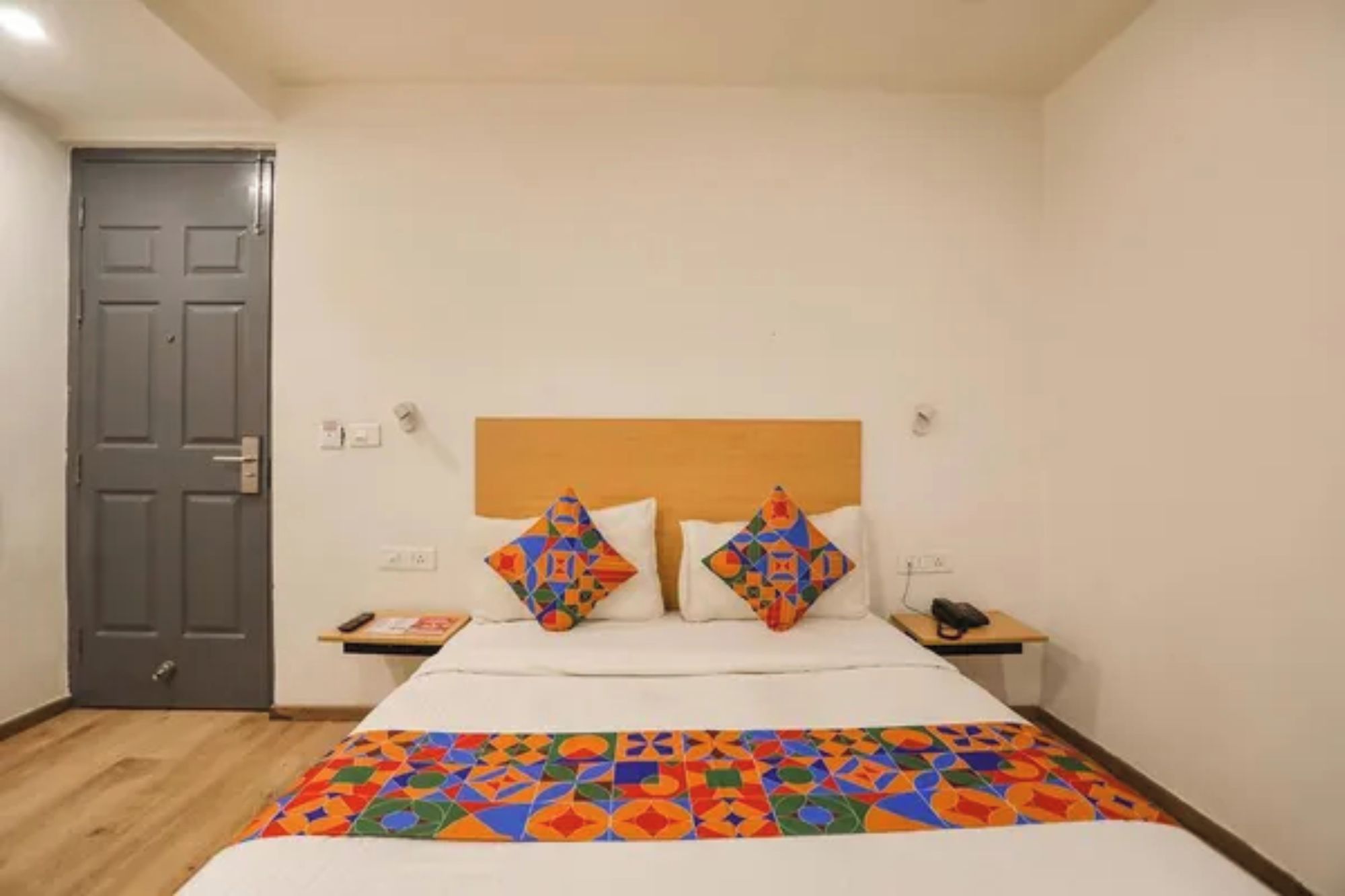 A hotel room with a bed, a wooden headboard, two bedside tables, and a door.