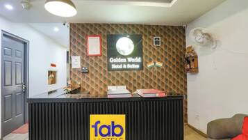 Un mostrador de recepción con un cartel de 'fab hotels', un cartel de 'Golden World Hotel & Suites' y un ventilador de pared.