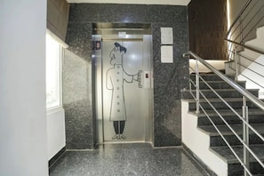 Un ascensor con una persona sosteniendo un teléfono, una escalera con barandillas de metal y una pared con una placa.