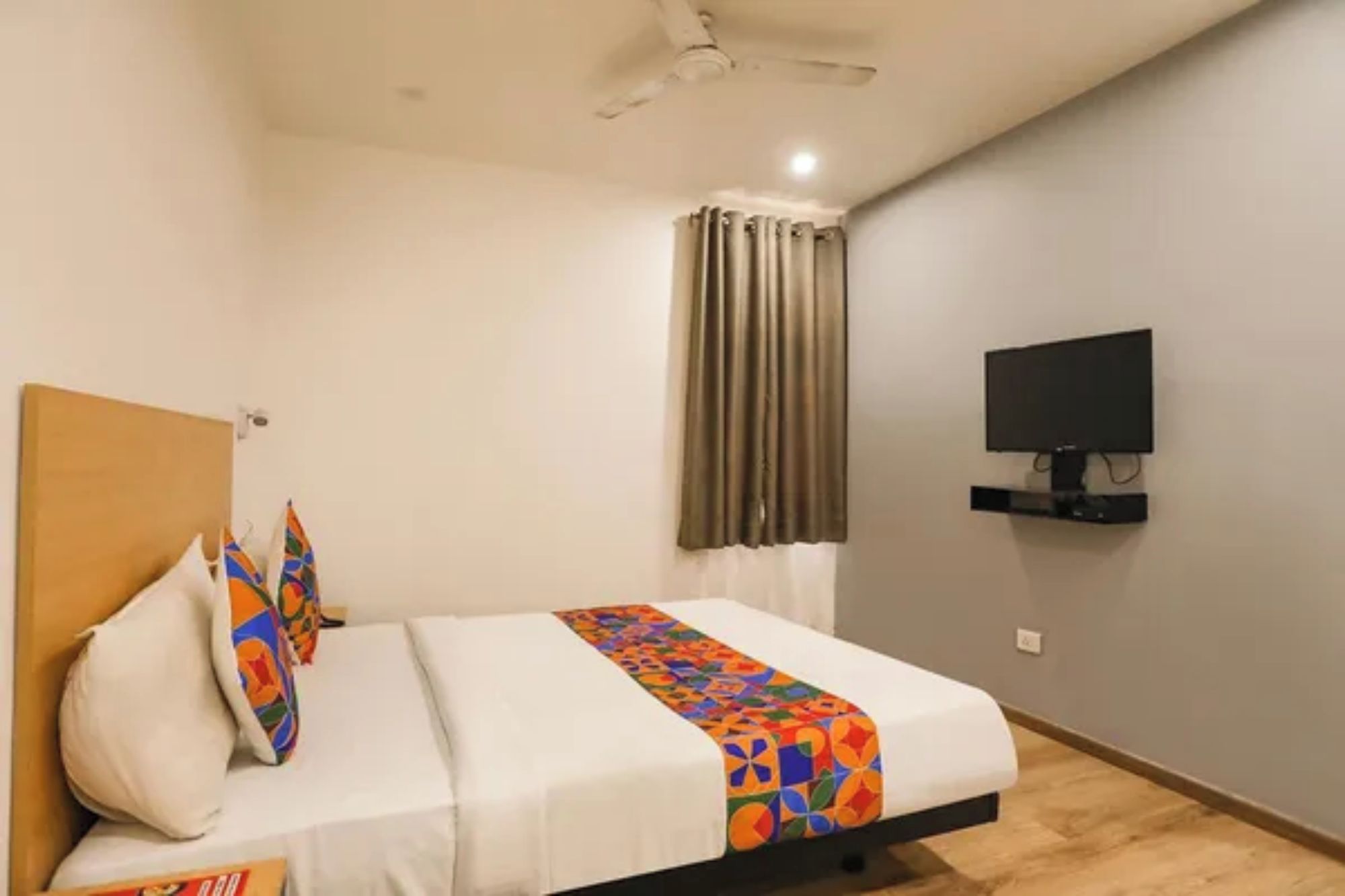 Ein Hotelzimmer mit einem Bett, einem an der Wand befestigten Fernseher und einem Deckenventilator.