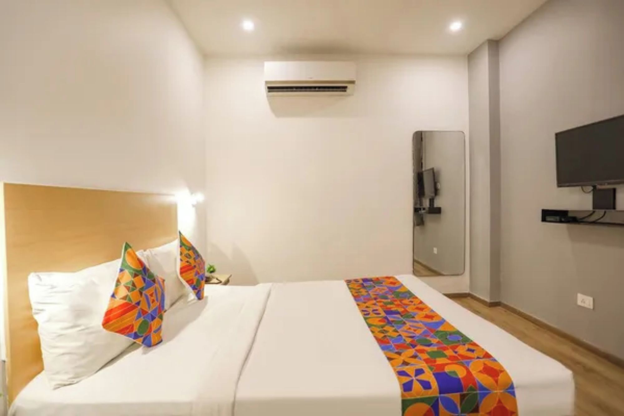A hotel room with a bed, a TV, an air conditioning unit, and a mirror.