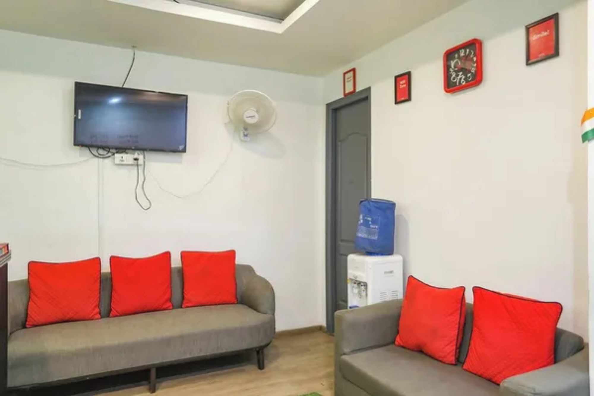 A living room with two sofas, a flat-screen TV, a wall-mounted fan, and a water dispenser.