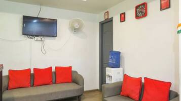 A living room with two sofas, a flat-screen TV, a wall-mounted fan, and a water dispenser.