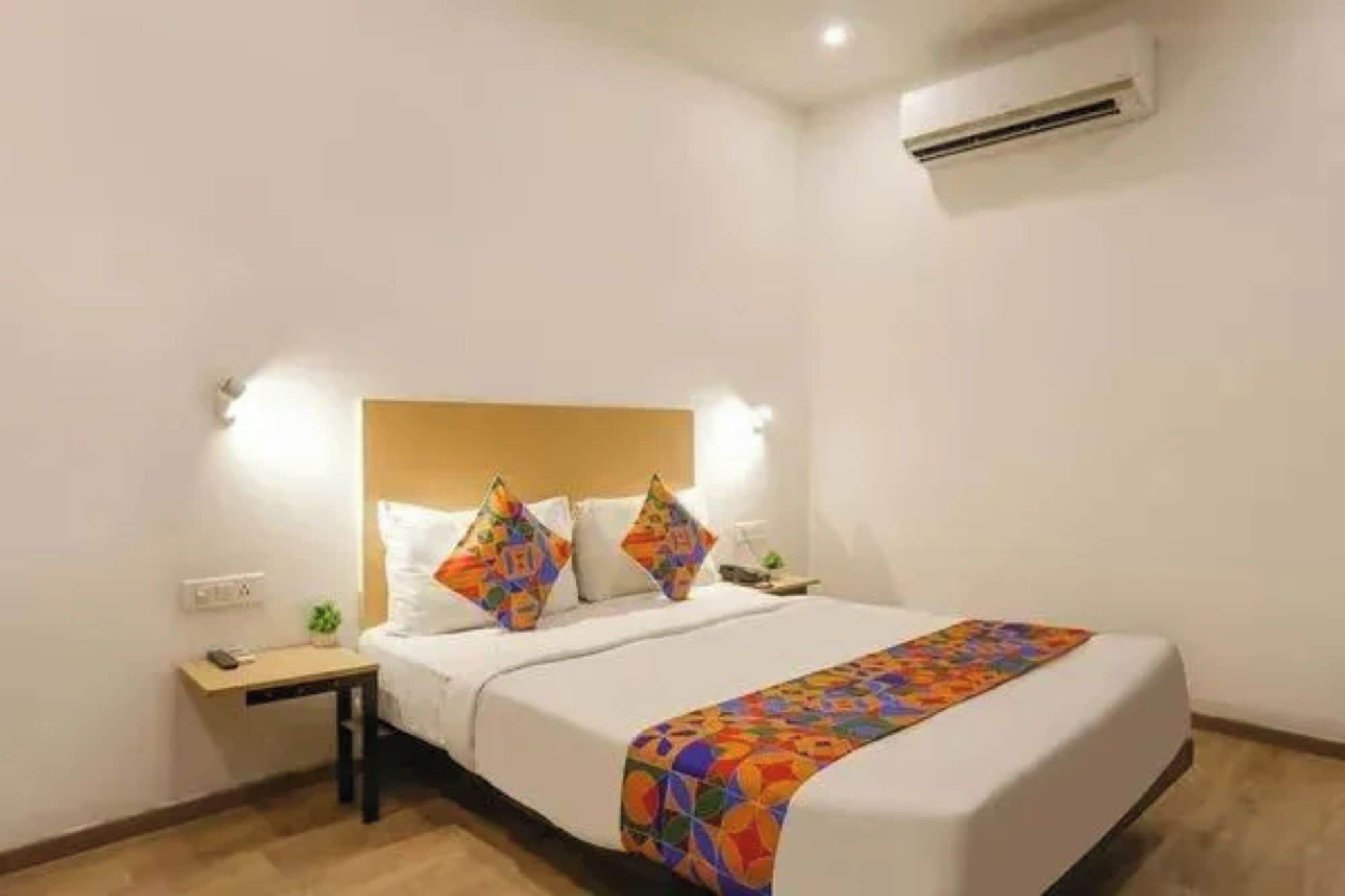 Una habitación de hotel con cama, mesita de noche y aire acondicionado.