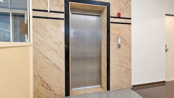 An elevator in a hallway with a marble wall and a tiled floor.