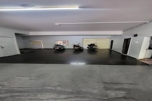 Zona interior àmplia amb un sòl de formigó polit, dues motocicletes estacionades al centre i una porta a l'esquerra.