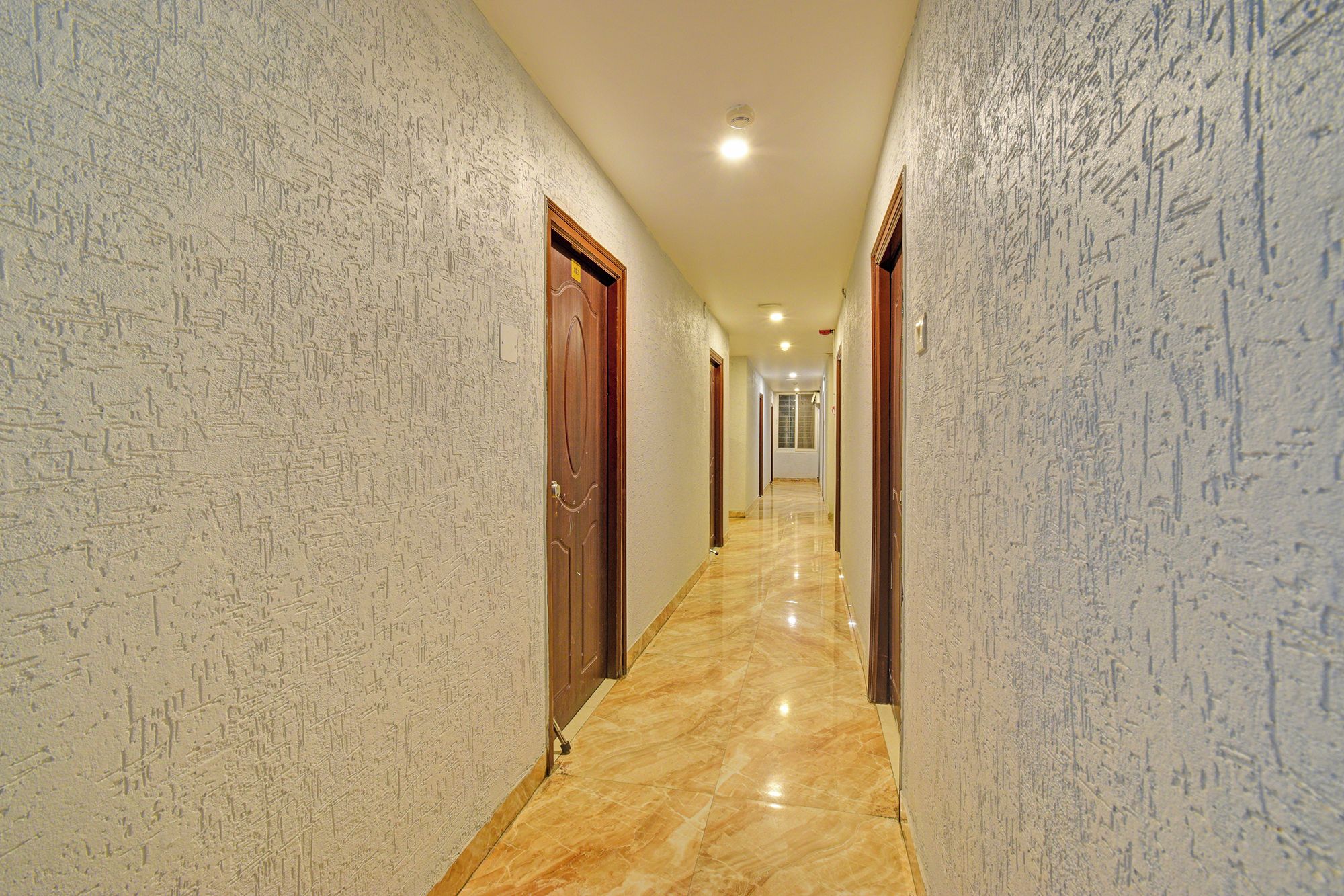 A corridor with patterned walls and a marble floor, leading to a door at the end.