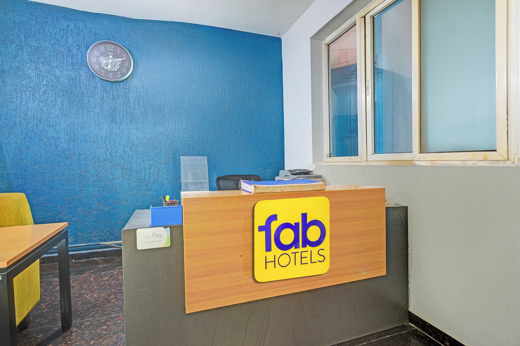 Ein Empfangsschalter mit einem 'Tab Hotels'-Schild, einer Uhr und einem Fenster mit Jalousien.