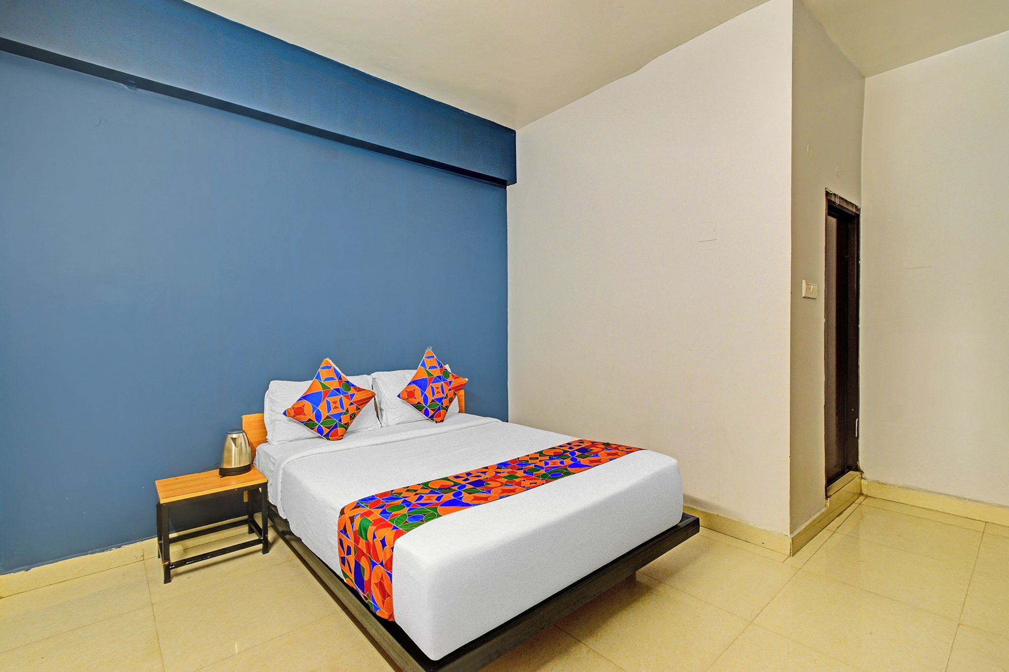 A hotel room with a bed, a nightstand, a lamp, and a door.