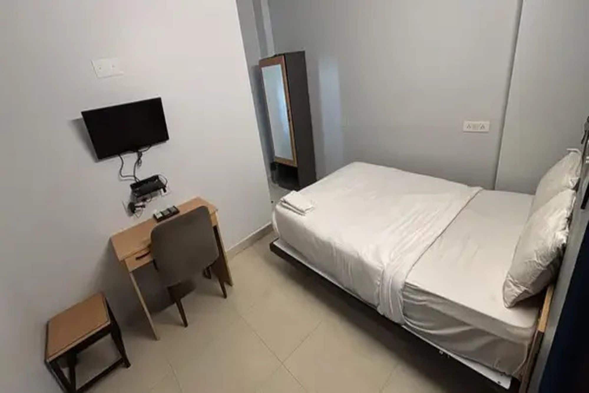 A bedroom with a bed, a desk, a chair, a television, and a wardrobe.