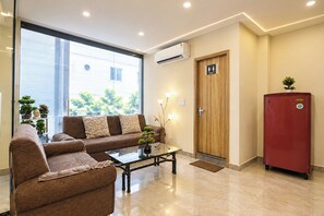 Quarto moderno com sofá, mesa de centro, geladeira vermelha e porta de madeira com a inscrição 'TOILET'.