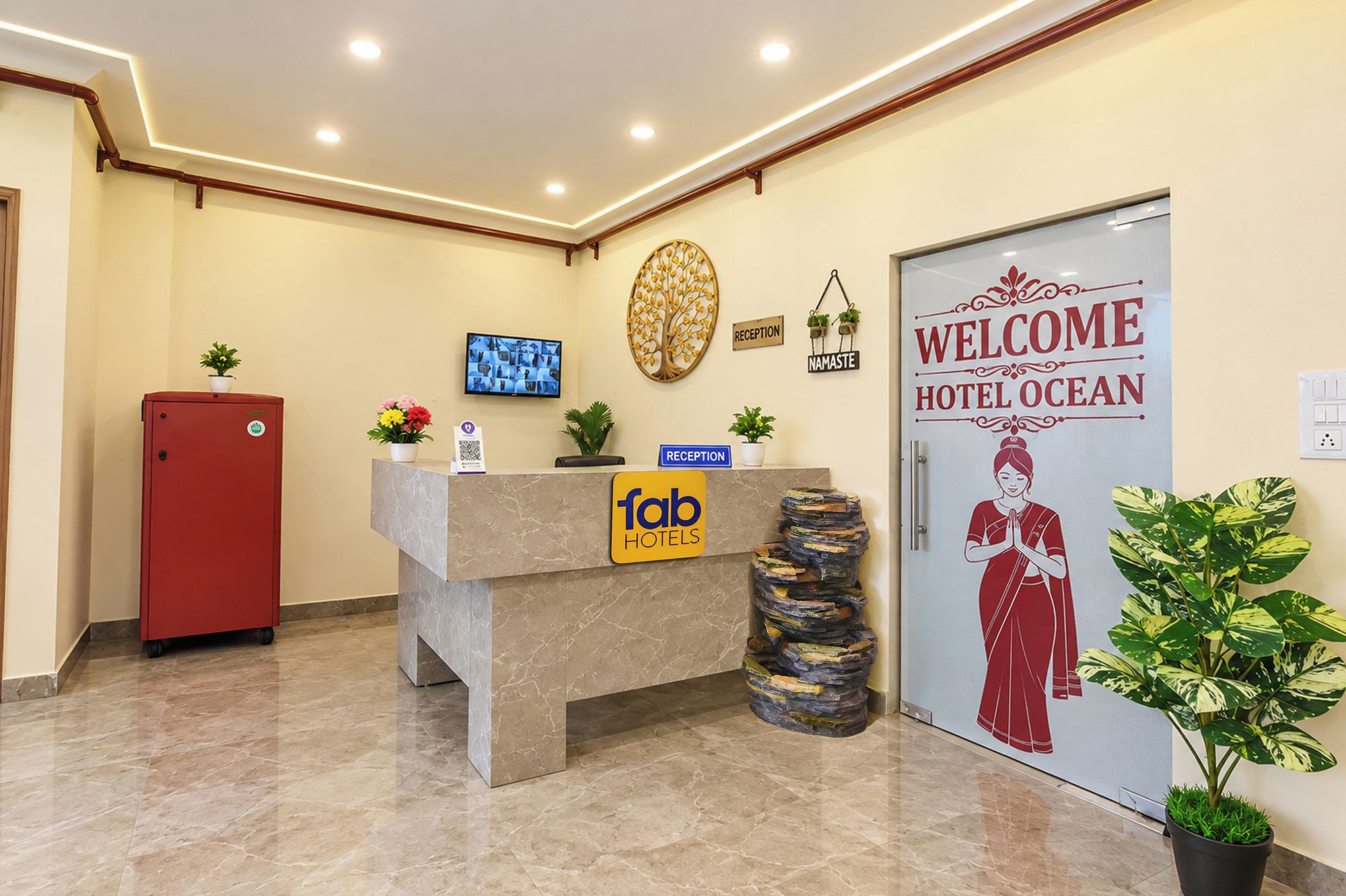 A hotel reception area with a reception desk, a red cabinet, a wall-mounted television, a 'Welcome Hotel Ocean' sign, and a 'Reception' sign.