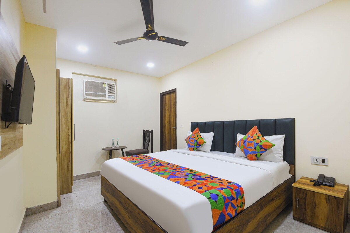 Quarto de hotel com cama, mesa de cabeceira, poltrona, ventilador de teto, ar condicionado e televisão na parede.