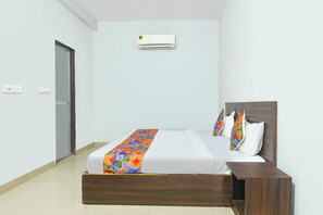 A hotel room with a bed, a nightstand, an air conditioning unit, and a door.