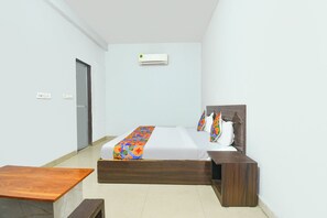 Una habitación de hotel con una cama, mesitas de noche, un escritorio, un equipo de aire acondicionado y una puerta.