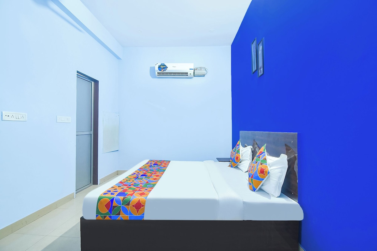 A hotel room with a bed, a window, an air conditioning unit, and a door.