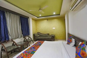 Una habitación de hotel con una cama, un sofá, una silla, un ventilador de techo y una ventana con cortinas.