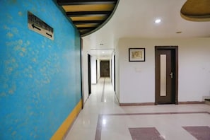 Un pasillo con pared azul, una señal con números de habitaciones, una puerta y un cuadro en la pared.
