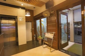 Vestíbulo de hotel con mostrador de recepción, puerta de entrada de vidrio y un cartel que indica que no se permite comida de fuera.
