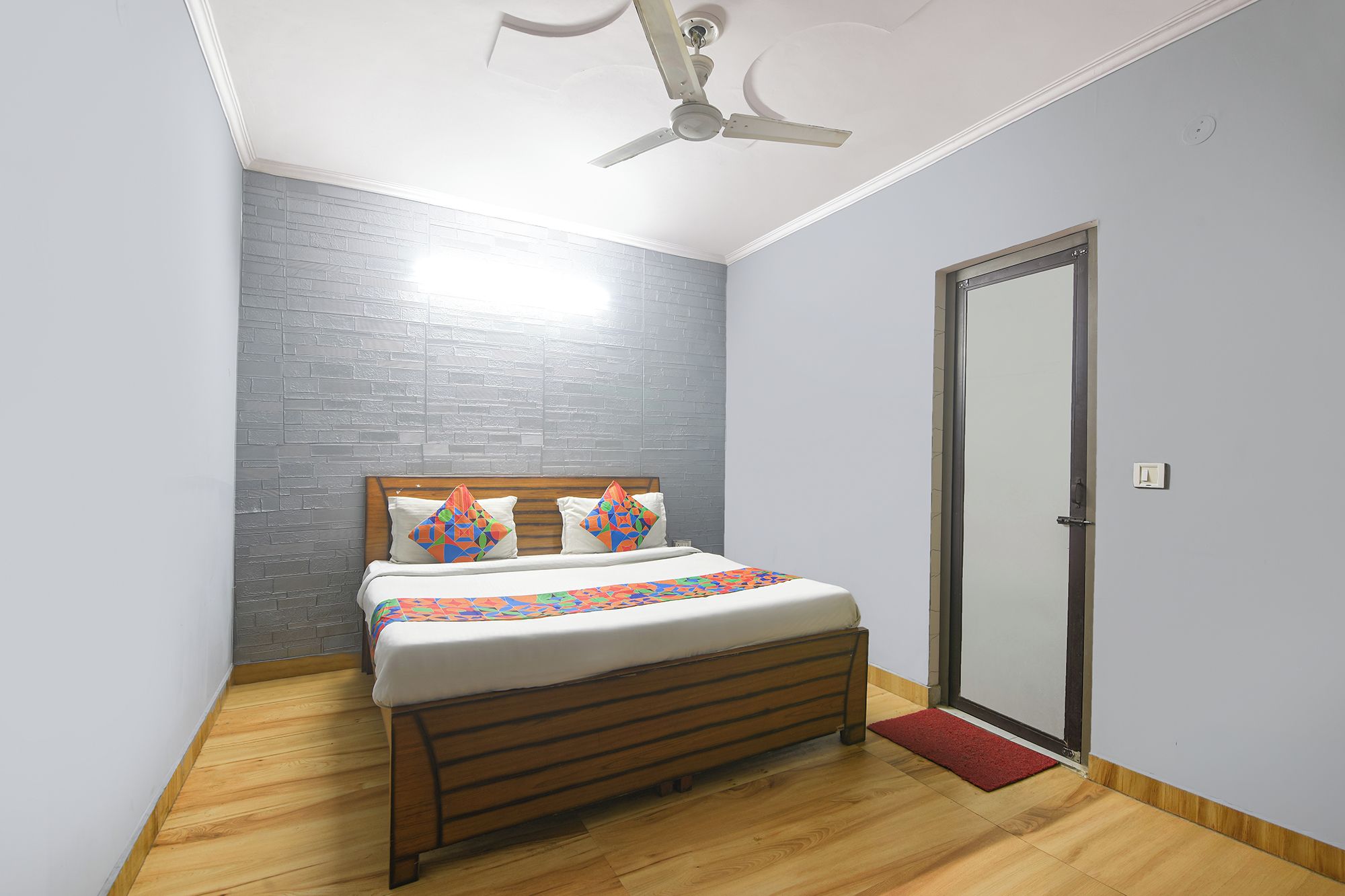 A bedroom with a bed, a ceiling fan, a door, and a brick-patterned wall.