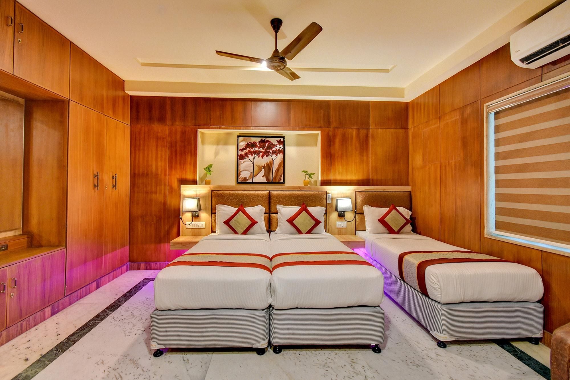 Habitación de hotel con paneles de madera, ventilador de techo, cama con cabecera, lámparas de noche y ventana con persianas.