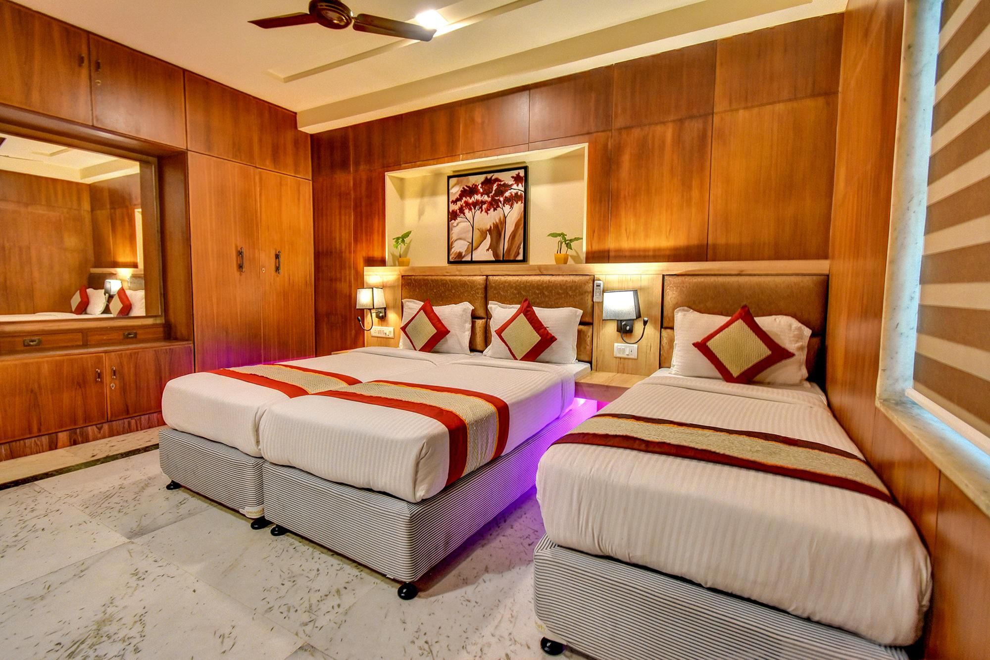 Habitación de hotel con dos camas, paneles de madera, ventilador de techo, un espejo grande y una obra de arte enmarcada en la pared.