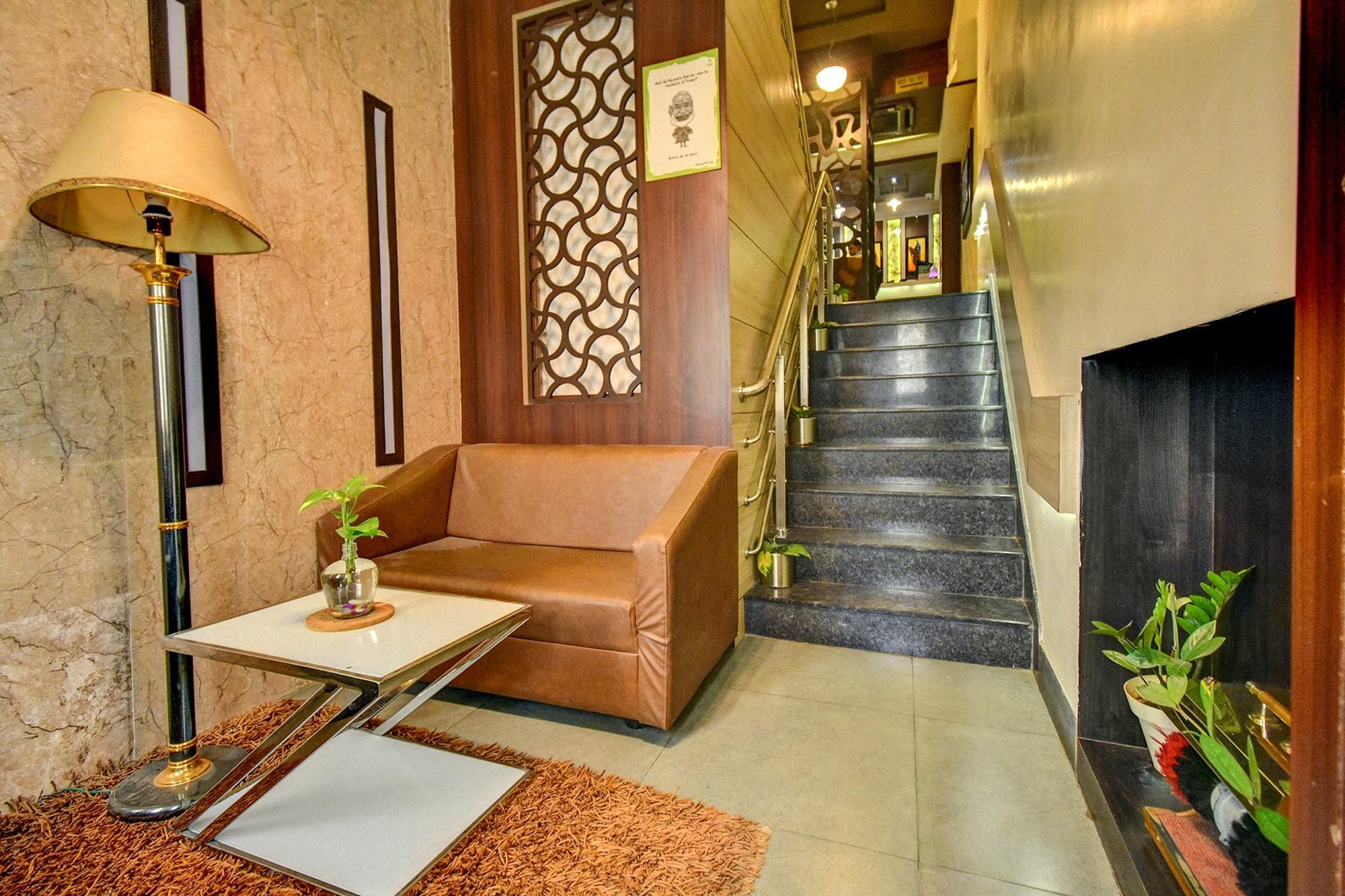 A hotel lobby with a sofa, a small table with a plant, a lamp, and a staircase.