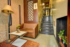 Eine Hotellobby mit einer Couch, einem kleinen Tisch mit Pflanze, einer Lampe und einer Treppe.