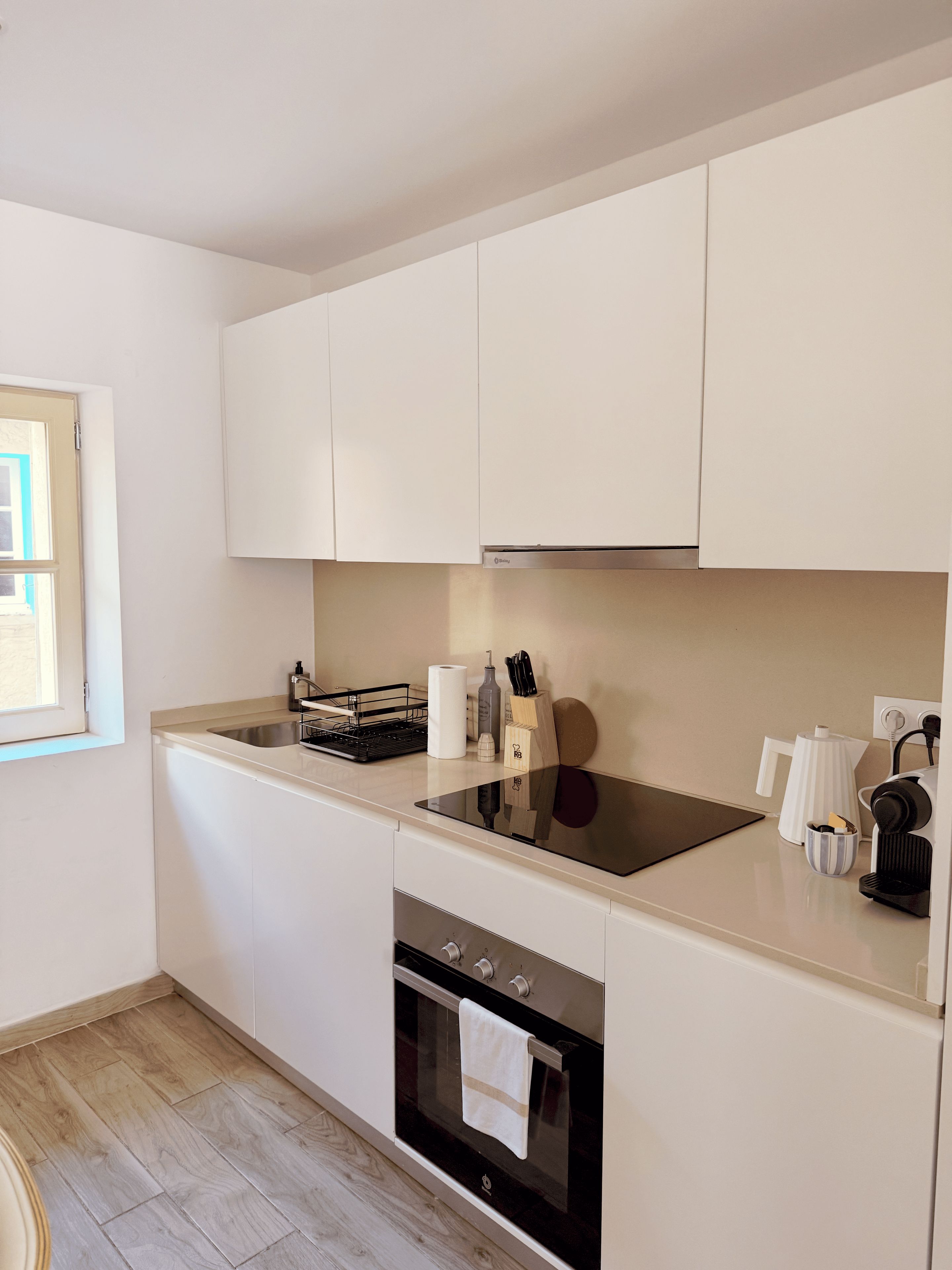 Una cocina moderna con armarios blancos, horno empotrado, placa de cocina y cafetera.