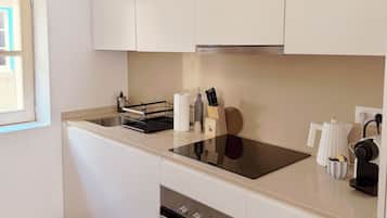 Una cocina moderna con armarios blancos, horno empotrado, placa de cocina y cafetera.