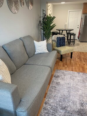 A living room with a grey sofa, a patterned rug, and a dining area with a table and chairs. - Good Life! (Charlotte)