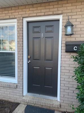 A residential house with a dark brown front door, a mailbox labeled 'C', and a window with blinds. - Good Life! (Charlotte)